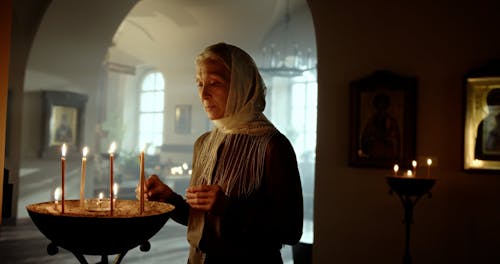 An Elderly Woman Lighting a Candle in a Church 