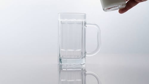 A Person Pouring Milk in a Glass Beer Mug 
