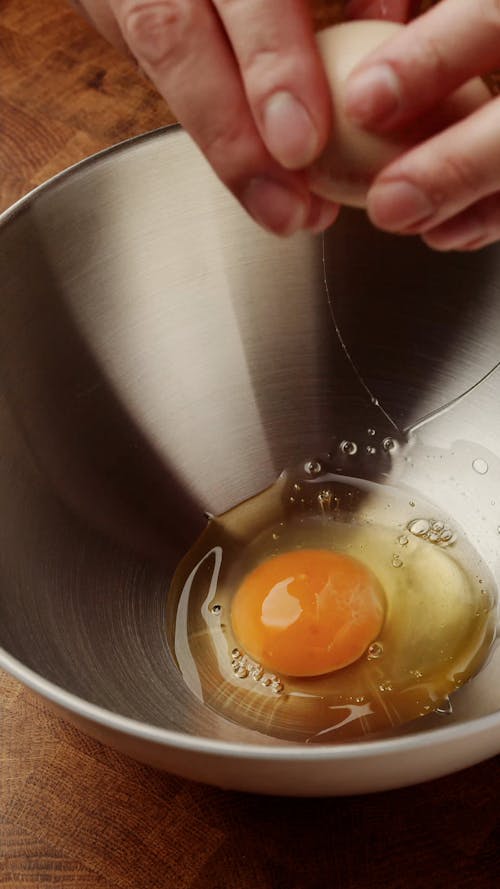 Person Breaking Eggs into Metal Bowl