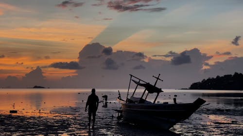 Silhouette of People near a Boat on a Beach at Sunset