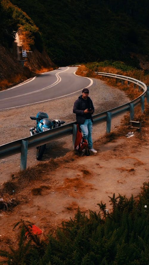 Man and Motorcycle Next to Road on Cliff