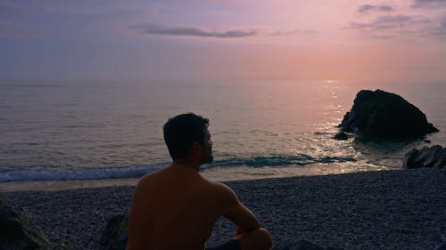 Back View of a Man Sitting on a Pebble Beach 