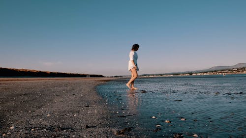 A Woman in a White Shirt Walking on an Empty Beach 