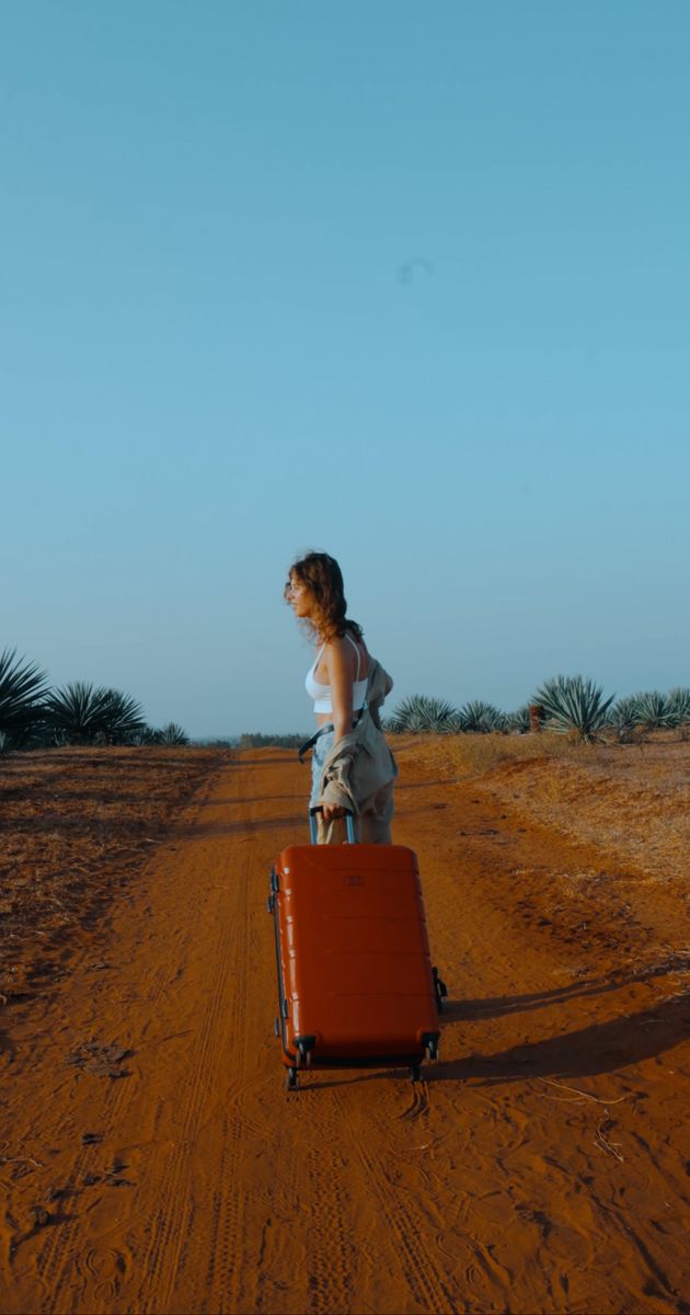 a woman walking with her suitcase on a dirt road 11760019