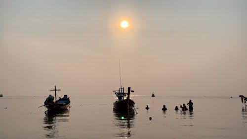 People Playing at the Seashore next to Anchored Fishing Boats