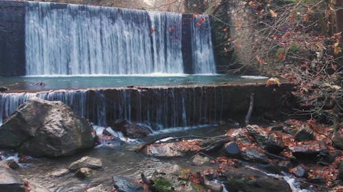 An Artificial Waterfall and a River Flowing through Mossy Rocks  