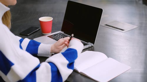 A Woman Taking Notes while Using a Laptop Computer