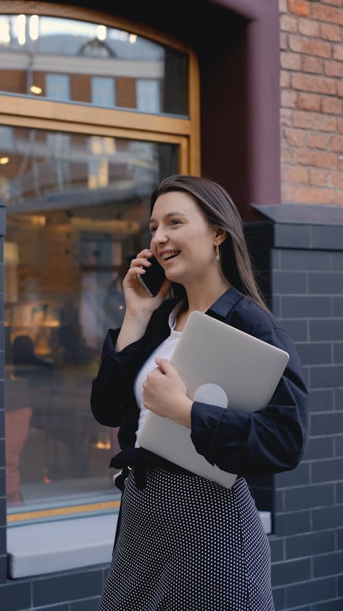 A Woman Carrying a Laptop while Talking on the Phone 