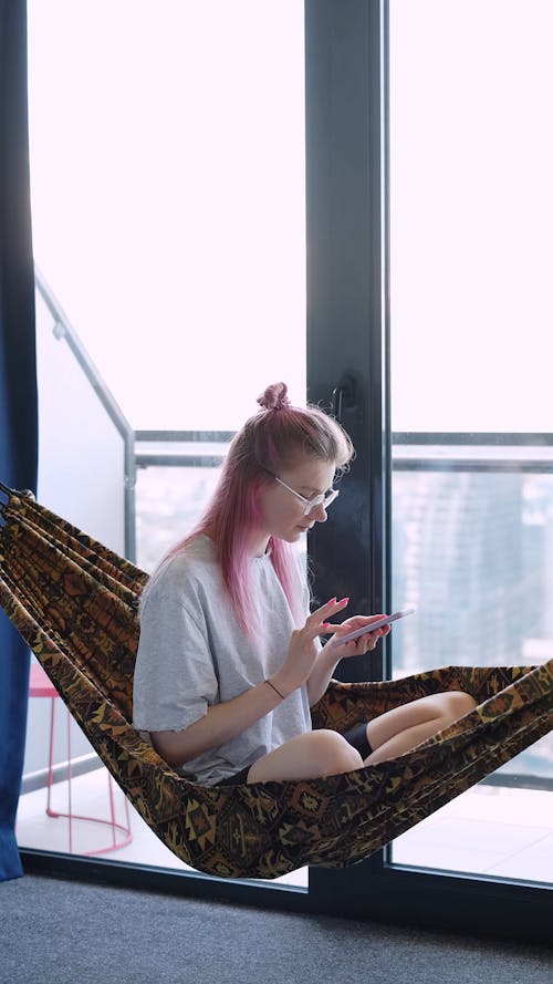 A Woman Making a Phone Call while Sitting in an Indoor Hammock