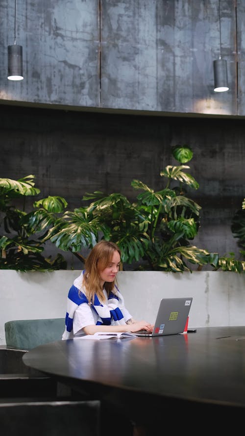 A Woman Sitting at a Table Using a Laptop and Drinking Coffee