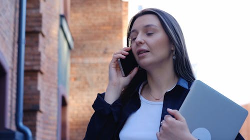 A Woman Talking on the Phone and Holding a Laptop in the Street