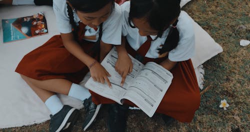 Two Schoolgirls Reading a Textbook During a Field Trip