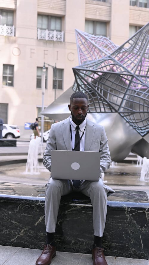 A Man Sitting by a Water Fountain while Working on his Laptop