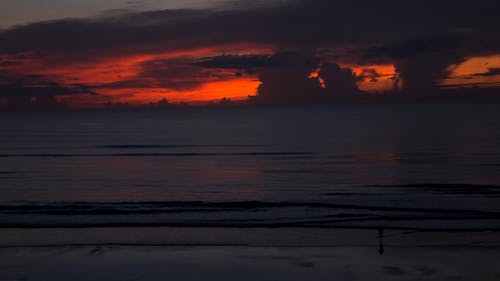 Silhouette of a Person Walking on the Beach under a Dramatic Sunset Sky 