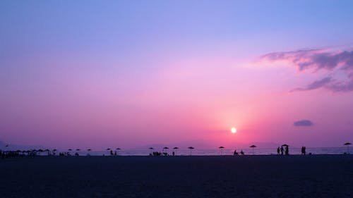 Silhouettes of People on the Beach under a Purple Sunset Sky 
