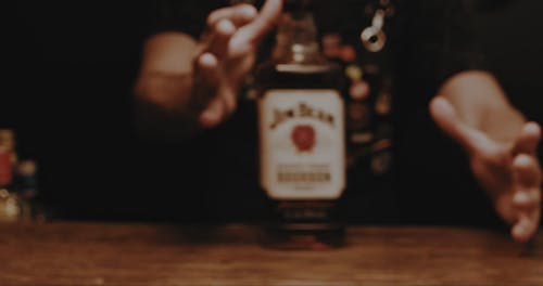 A Barman Sliding a Bottle of Whiskey on the Bar Counter