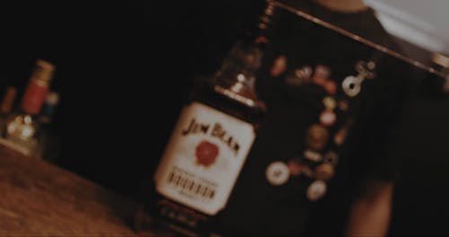 A Barman Grabbing a Bottle of Whiskey from the Bar Counter