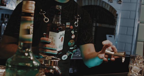 A Barman Holding a Whiskey Bottle and a Jigger 