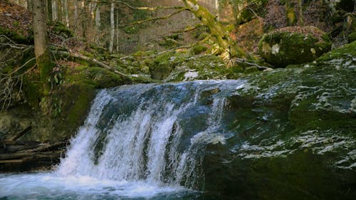 A Waterfalls Cascading on River Between Mossy Rocks