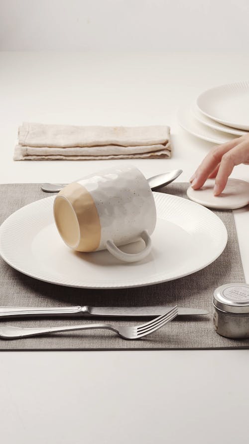 A Person Removing a Mug Lid from a Set Table 