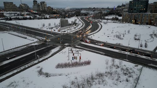 A Drone Footage of Moving Cars on the Road Between Buildings on a Snow Covered Ground