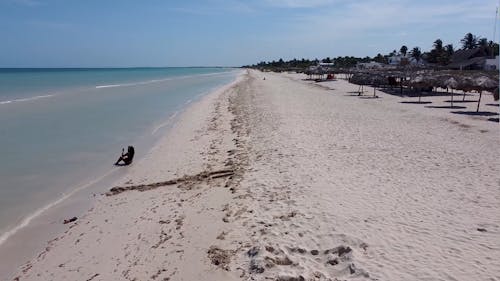 A Drone Footage of a Person Sitting on the Beach Sand