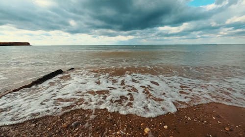 A Beach Waves Crashing on Shore Under the Cloudy Sky