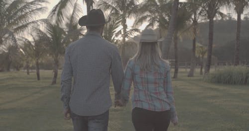 Couple Running in the Grass Field While Wearing Cowboy Hats
