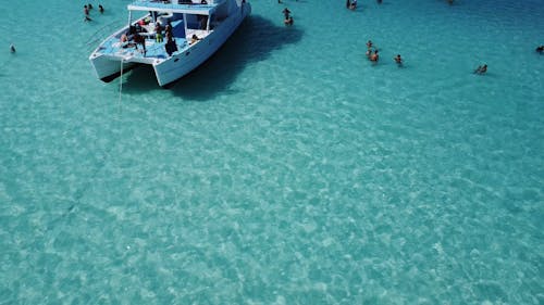 A Drone Footage of a Yacht on the Sea Near the People Swimming on the Beach