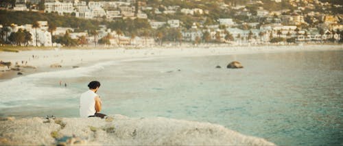 Back View of a Man Sitting on the Rocks near the Ocean 