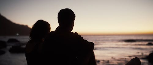 Silhouette of two people enjoying the sunset after golden hour on a rock in front of the ocean