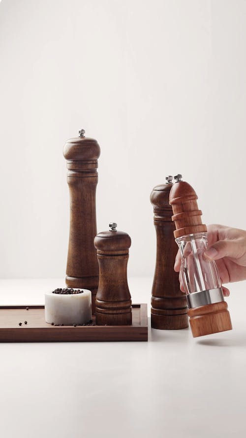 A Person Placing Pepper Mills on a White Surface 