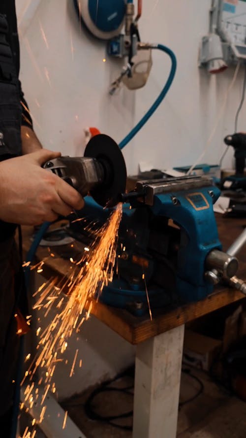 A Person Using an Angle Grinder and a Vise to Cut a Metal Piece