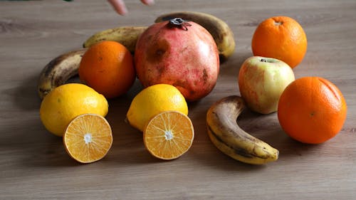 A hand reaching for medicinal fruits consisting of red pomegranate, ripe banana, yellow lemon and orange orange