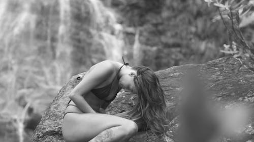 A Young Woman in a Bikini Posing on a Rock by a Waterfall