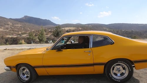 A Couple in a Yellow Car Driving by an Aqueduct in a Mountain Landscape