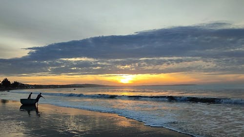 Two Men Pulling a Wooden Boat into the Sea at Sunset