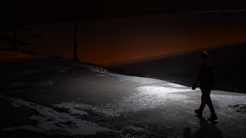 A Person Walking on a Snowy Road at Night 