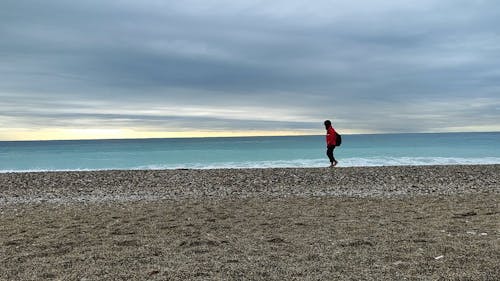A Person Walking on the Beach on a Cloudy Day