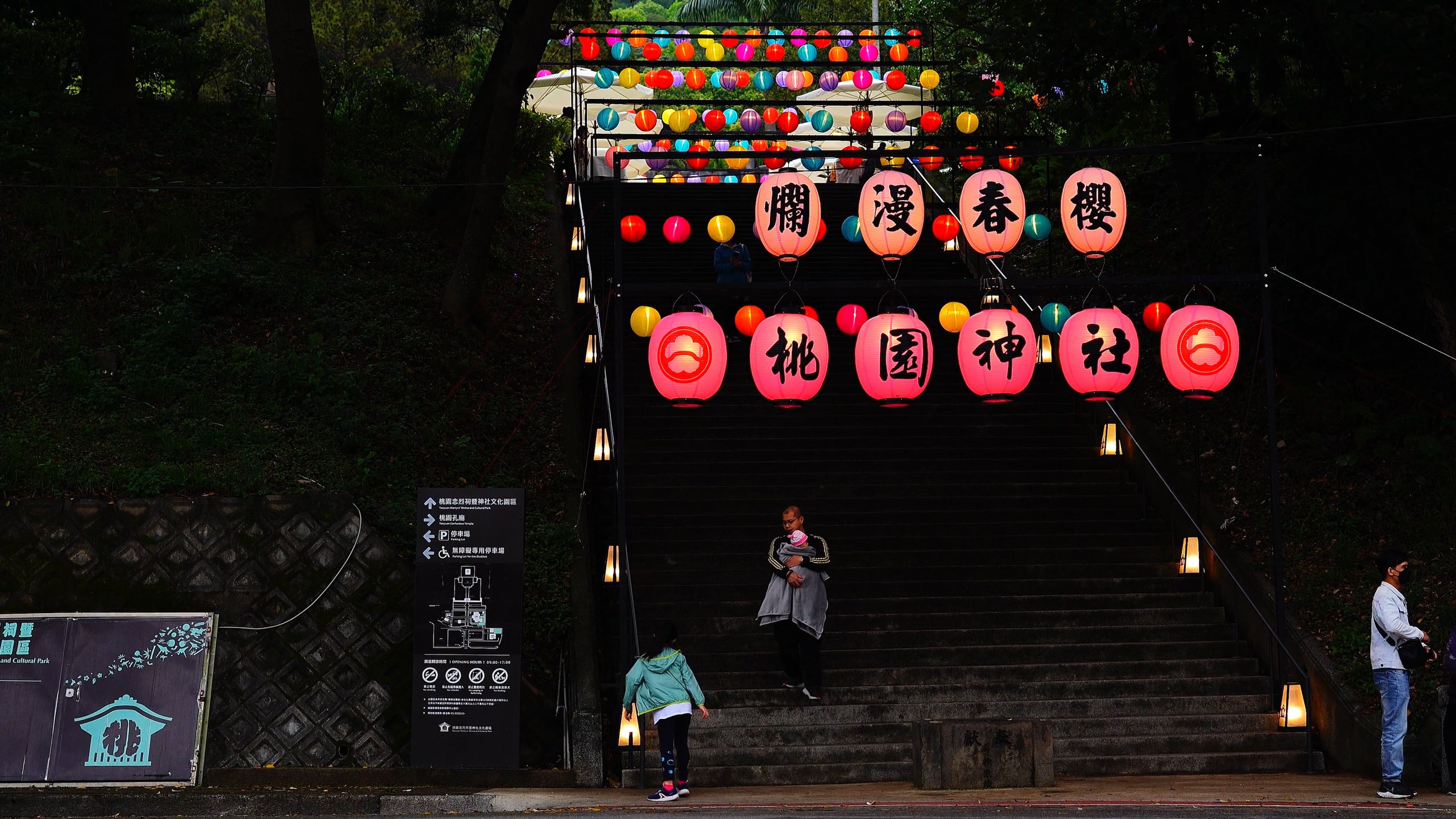 A group of people walking up a set of stairs with lanterns hanging from ...