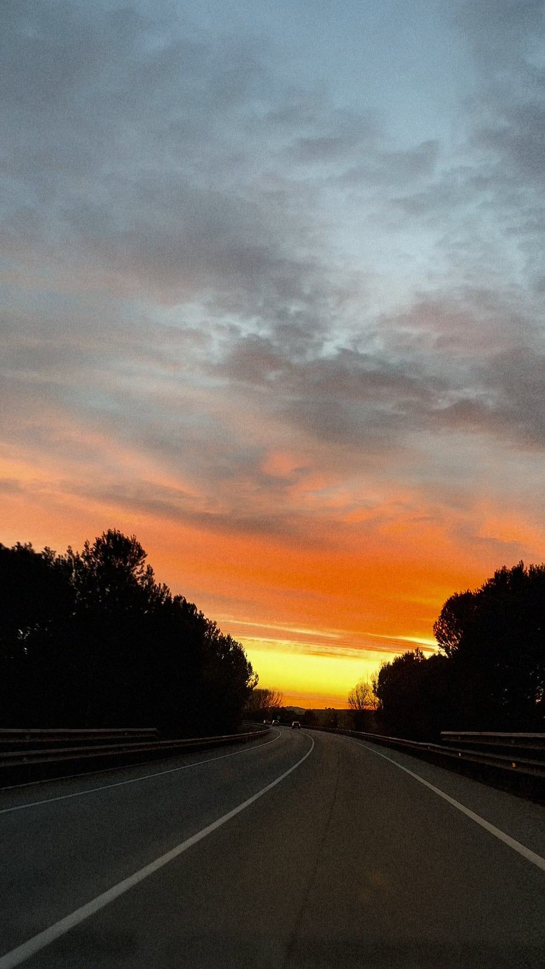the sun sets over a highway with a car driving on it 16120020