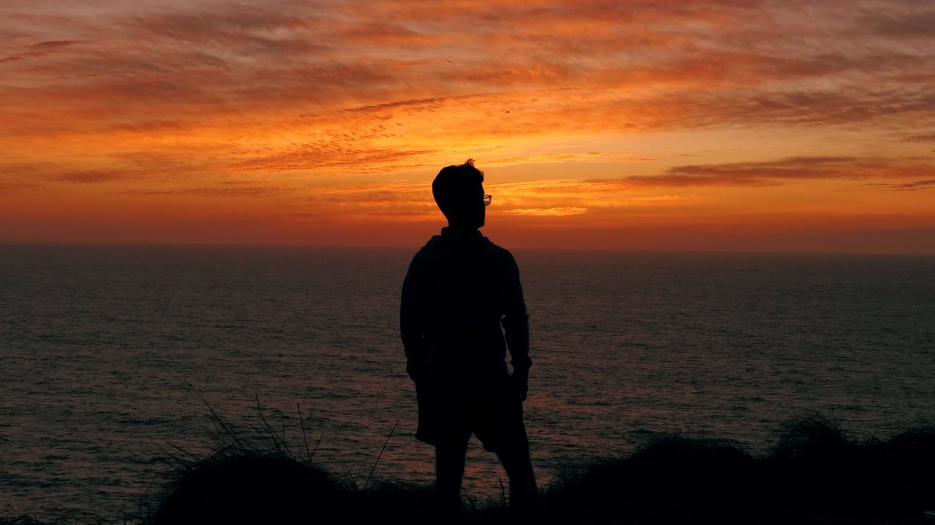 A silhouette of a person standing on a cliff overlooking the ocean Free ...