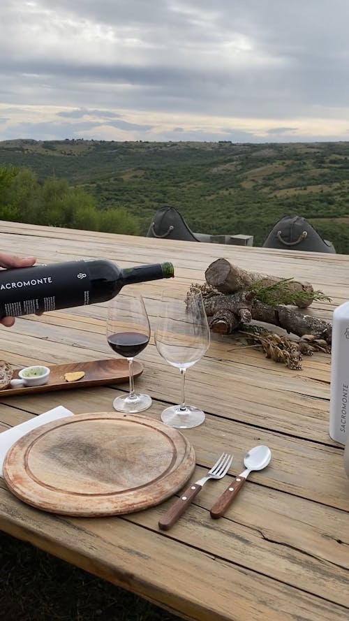A Person Pouring Red Wine into a Glass at an Outdoor Table 
