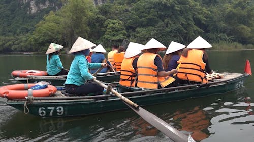 People in Life Jackets and Conical Hats Taking a Boat Ride 