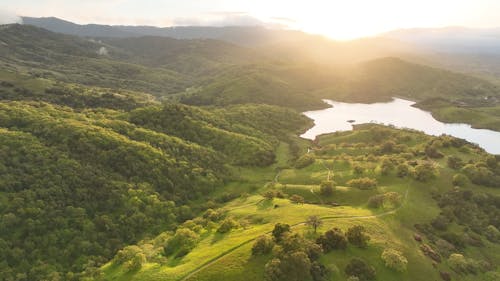 Drone Footage of a Lake among Green Hills at Sunrise 