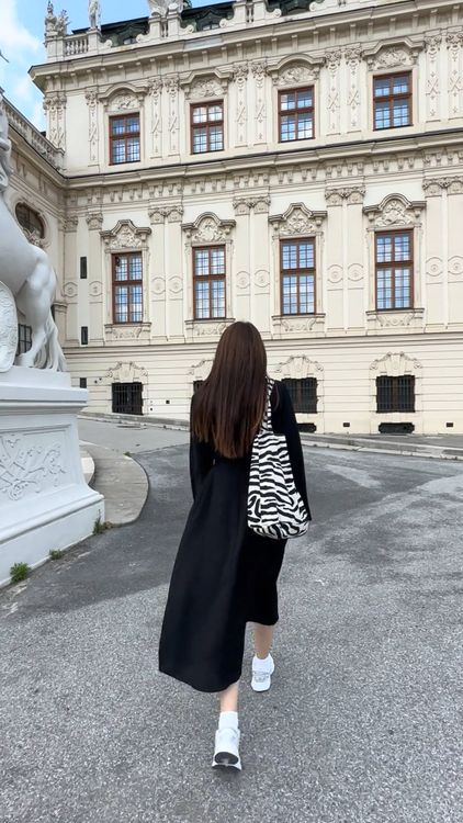 A woman walking down a street in front of a large building Free Stock ...