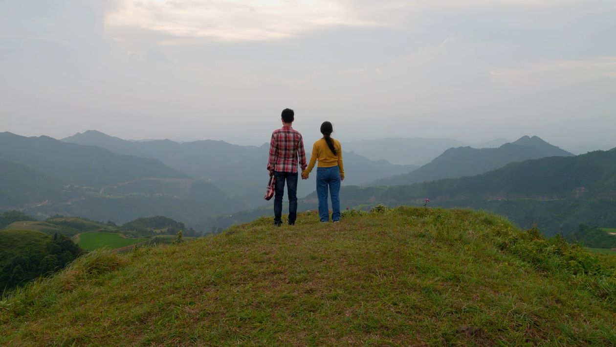 Two people standing on top of a hill looking at the mountains Free ...