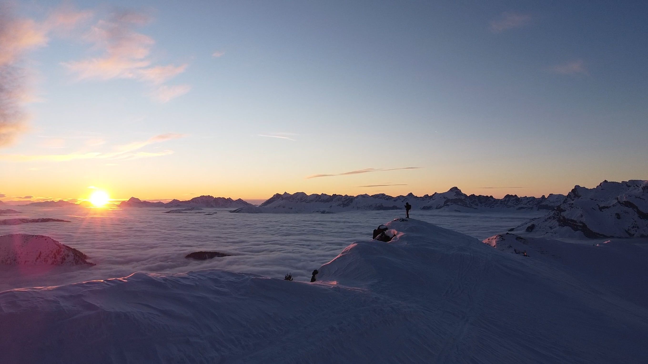 A person standing on top of a mountain with the sun setting behind them ...
