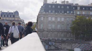 people walking on a bridge in front of buildings
