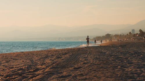 Fixed shot at the beach near the coastline of Marbella, Spain. Man running in silhouette and people scattered on the background. Empty sandy foreground.